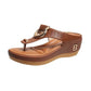 Brown faux leather wedge thong sandals featuring a decorative gold-tone ring, perforated strap detail, and a straw-effect wedge with a contoured footbed. These comfortable summer sandals offer a stylish elevated look.