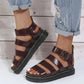 A pair of deep burgundy PU leather gladiator sandals with a chunky black platform sole and yellow stitching, worn by a person in cuffed denim jeans.