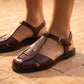 Rich burgundy woven vegan leather fisherman sandals featuring a T-strap and gold-tone buckle, worn on feet against a warm tiled background.