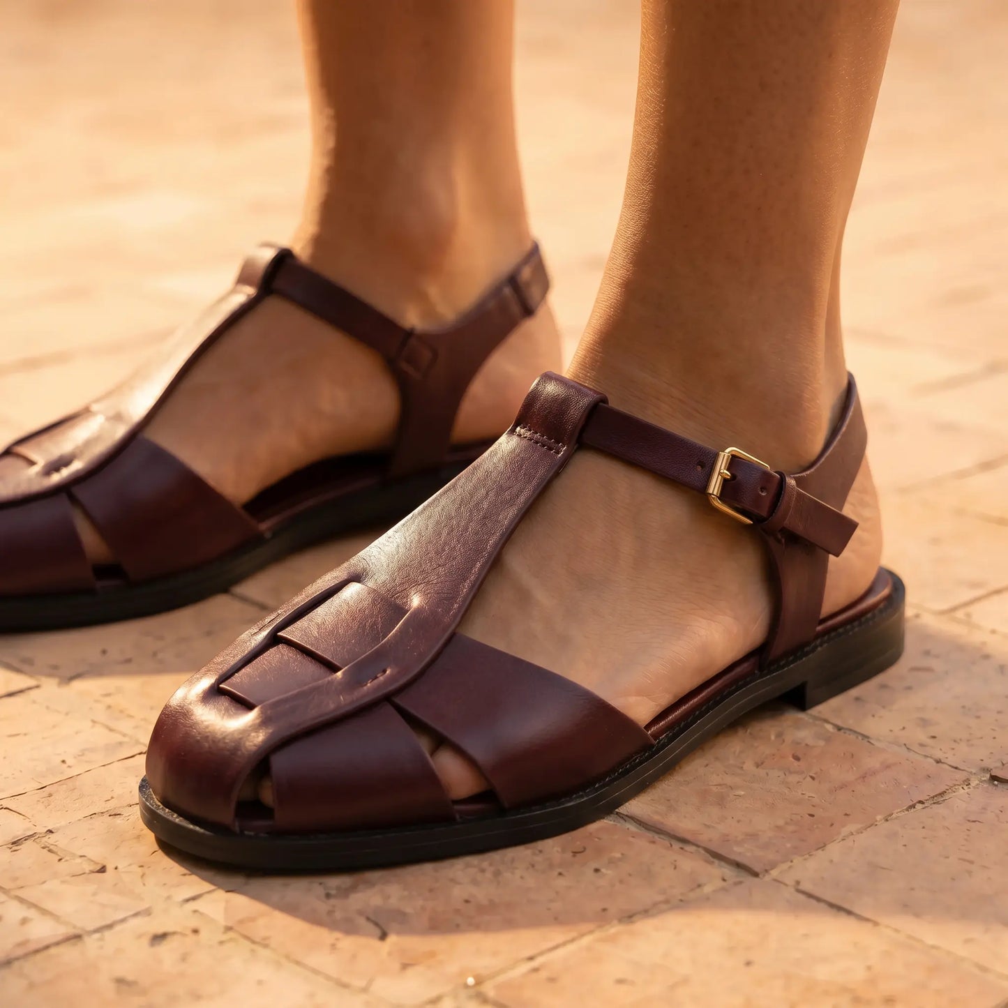 Rich burgundy woven vegan leather fisherman sandals featuring a T-strap and gold-tone buckle, worn on feet against a warm tiled background.