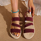 Close-up of women's burgundy woven elastic strap flat sandals with a fish-mouth open toe, worn on feet with a turquoise beaded ankle bracelet and chic rings.