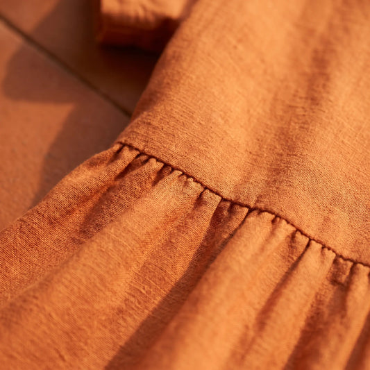 Detailed view of Kivori burnt orange linen-cotton blend midi dress fabric, showing textured slub lines and delicate gathering at the empire waist.