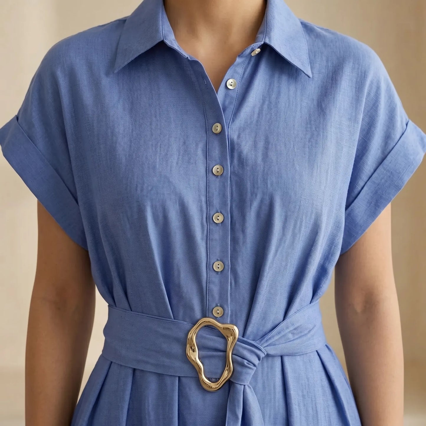 Close-up of the Zivro chambray blue linen-blend midi dress, highlighting the structured point collar, delicate pearlescent buttons on the placket, cuffed short sleeves, and the distinctive gold organic-shaped buckle on the wide fabric belt.