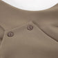 Close-up of a chic beige vest featuring an asymmetrical crossover detail with two small matte buttons at the shoulder area, showcasing fabric texture.
