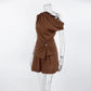 Chocolate brown linen-blend two-piece set featuring an asymmetrical one-shoulder top with draped bodice and gold-tone buckle, paired with high-waisted shorts.