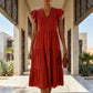 Elegant woman wearing a classic red tiered midi dress with a V-neck and ruffle cap sleeves, showcasing its flowing A-line silhouette in a stylish outdoor walkway.