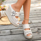A woman's feet wearing elegant cream woven wedge sandals with peep-toe design and dual buckle straps, set against a rustic wooden deck background.