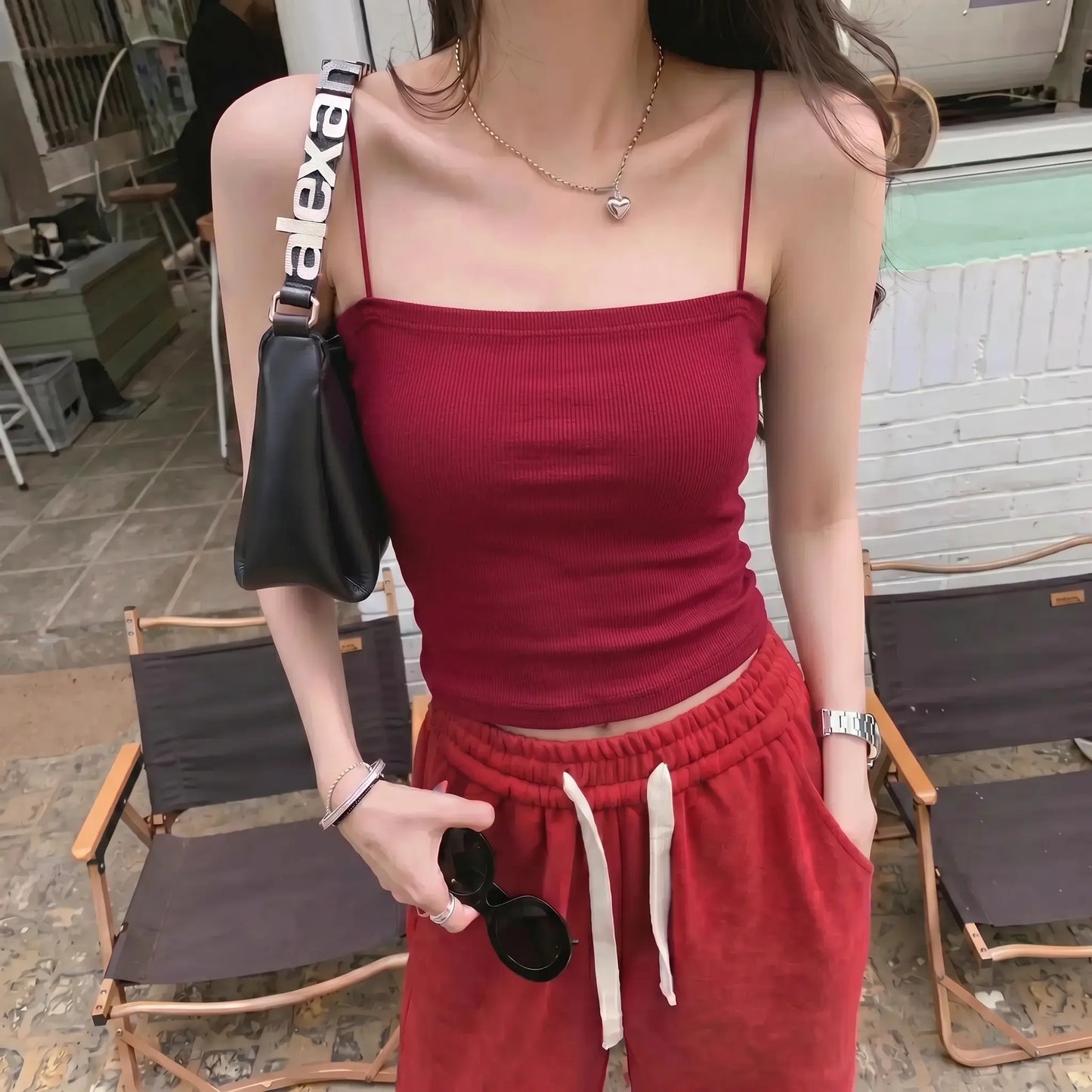 Model wearing a Miroka crimson red camisole top with thin spaghetti straps and a straight neckline, featuring a fine ribbed texture. Paired with red bottoms in an outdoor setting.