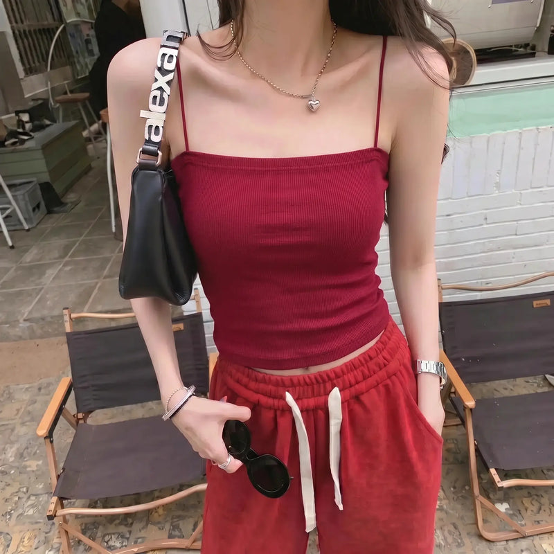 Model wearing a Miroka crimson red camisole top with thin spaghetti straps and a straight neckline, featuring a fine ribbed texture. Paired with red bottoms in an outdoor setting.