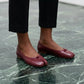 Crimson red vegan leather split-toe ballet flats with a delicate bow, worn by a model on a green marble floor, showcasing their elegant design.