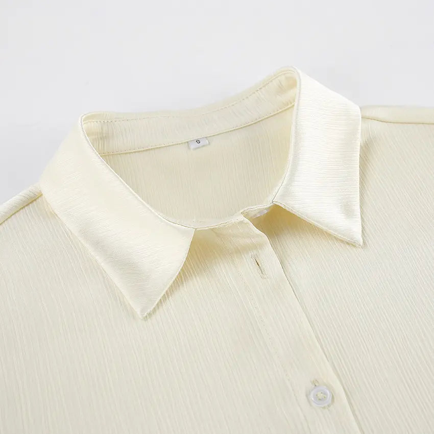 Close-up of the Tarkem crinkle pleat shirt in ivory buttercream, highlighting the classic pointed collar, tonal front button, and the distinctive textured fabric.