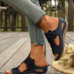 Woman's feet wearing comfortable dark blue wedge sandals with intricate floral laser-cut details, paired with casual denim jeans on a wooden deck.