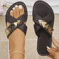 Dark brown flat cross-strap sandals adorned with layered mixed-metal triangular embellishments and clear rhinestones, shown on a model's foot with white toenails and a delicate anklet. These chic slides feature white contrast stitching on the sole.