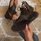 Woman wearing dark brown matte PU leather gladiator flat sandals with a thong toe, lace-up ankle ties, and white contrast sole stitching, styled with denim jeans.