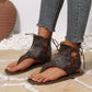Dark brown matte PU leather gladiator sandals with a thong toe and intricate lace-up detailing up the ankle, worn with frayed denim jeans.