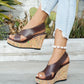 Women's dark brown criss-cross strap wedge sandals with a multi-color speckled cork platform and wedge, shown worn on feet with light wash denim jeans.