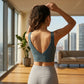 Dark teal Zykari V-back yoga sports bra on woman, seen from behind, highlighting the deep V-cut and wide straps in a modern apartment.