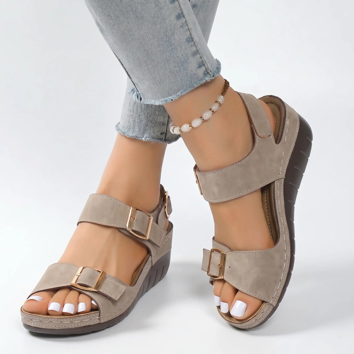 Desert Khaki faux suede wedge sandals with gold buckles and contrast white stitching, shown on a model's feet with casual jeans and an anklet.