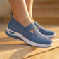 Dusty Blue Ruxen slip-on sneakers on a model, showing breathable woven knit, diamond perforations, and a triangular instep cutout. White platform sole on stone steps.