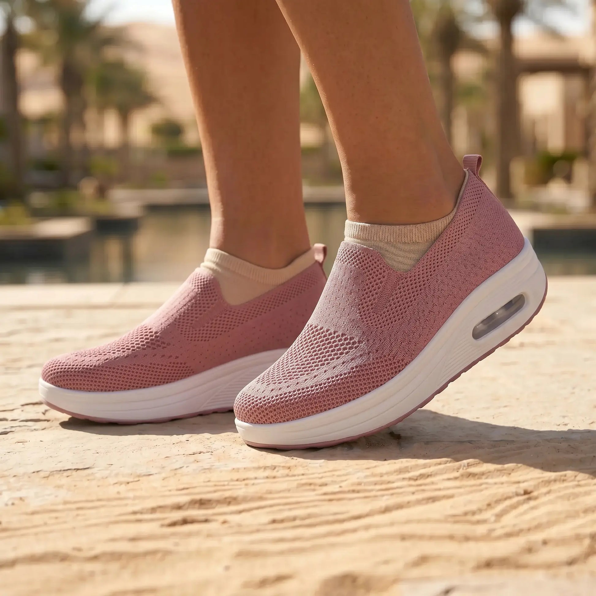 A pair of Myrkos Dusty Rose knit slip-on sneakers worn by a model, standing outdoors on a textured surface. The sneakers feature a white platform sole with a visible air cushion and a perforated knit upper.