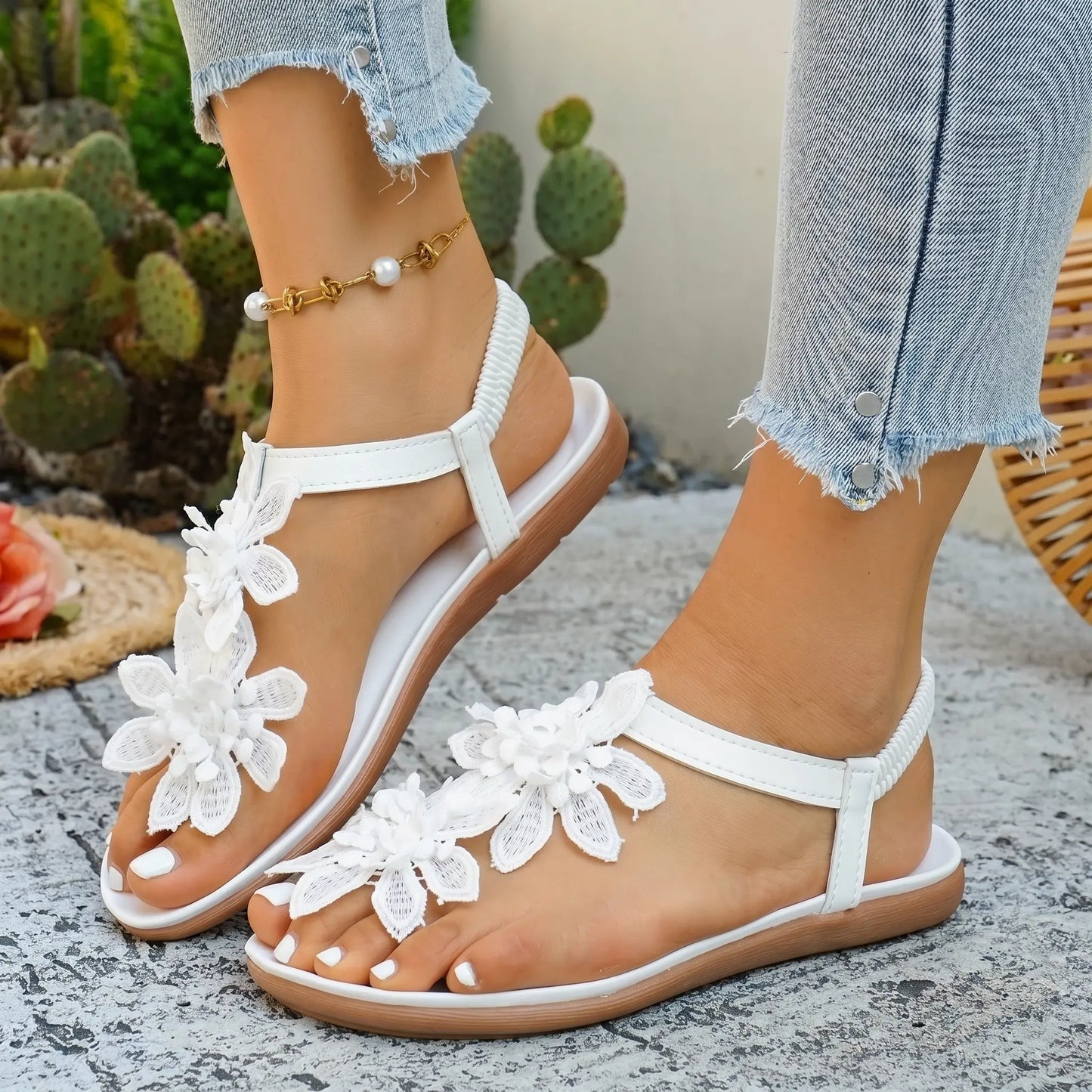 Women's white flat thong sandals featuring delicate layered fabric floral embellishments on the vamp and a comfortable elasticated slingback strap, styled for a bohemian summer look.