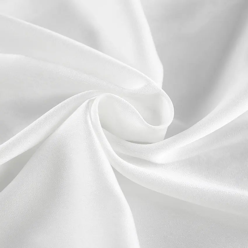 Close-up view of flowing ivory satin-like fabric with delicate folds, showcasing its subtle sheen and luxurious drape, perfect for elegant loungewear or resort wear.