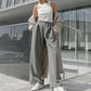Woman wearing elegant grey wide-leg trousers with sharp front pleats and a fluid drape, styled with a white tank top and beige trench coat.