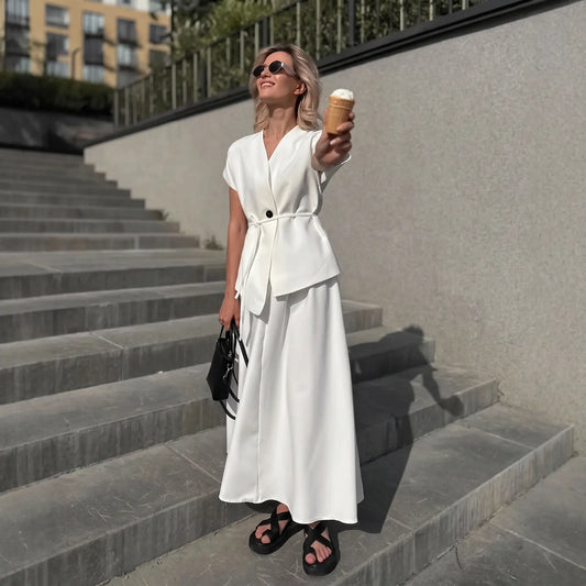 Woman wearing an elegant white two-piece set featuring a sleeveless V-neck top with a tie belt and an A-line midi skirt, standing on outdoor stairs while holding an ice cream cone.