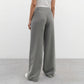 Back view of elegant wide-leg trousers in sophisticated grey, featuring a high waist, fluid drape, and straight, flowing legs, shown on a minimalist white background.