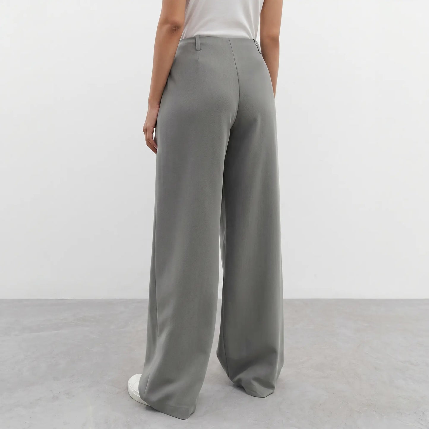 Back view of elegant wide-leg trousers in sophisticated grey, featuring a high waist, fluid drape, and straight, flowing legs, shown on a minimalist white background.