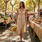 Elivora sleeveless linen midi dress in beige with button-down front and pockets, worn by a woman at a sunny outdoor market.