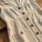 Close-up of Elivora linen midi dress in beige, showing wood-style buttons, V-neckline, and deep patch pockets on textured fabric.