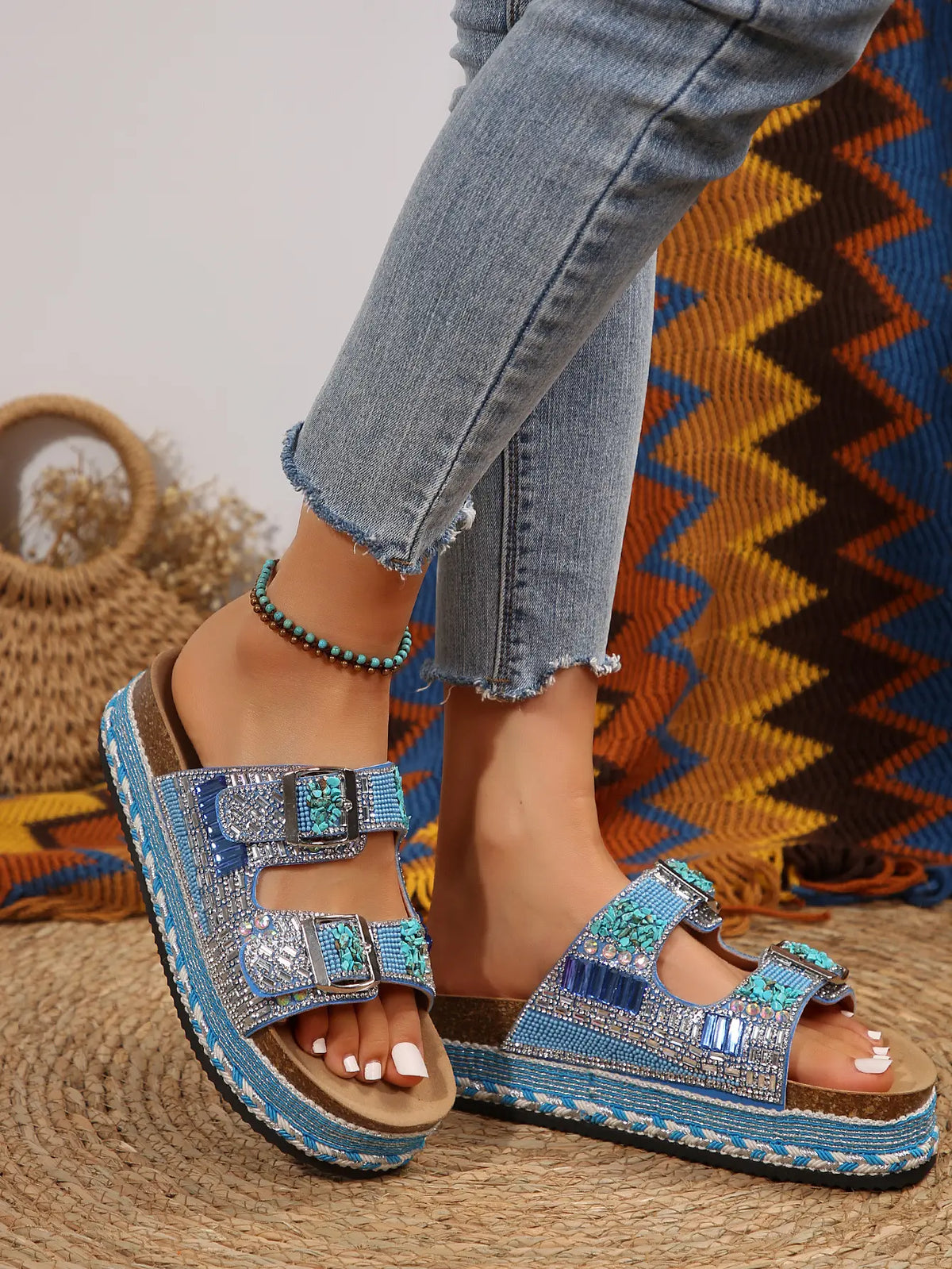 Bohemian-inspired platform slide sandals embellished with rhinestones, blue, pink, and turquoise stones, worn by a model with frayed jeans and an anklet.