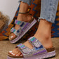 Woman's feet wearing embellished platform slide sandals with purple straps, rhinestones, beads, and blue resin stones, paired with denim jeans.