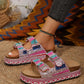 Embellished platform slide sandals with double buckle straps, adorned with dazzling rhinestones, pink beads, and turquoise resin stones, worn on a foot with a bohemian backdrop.
