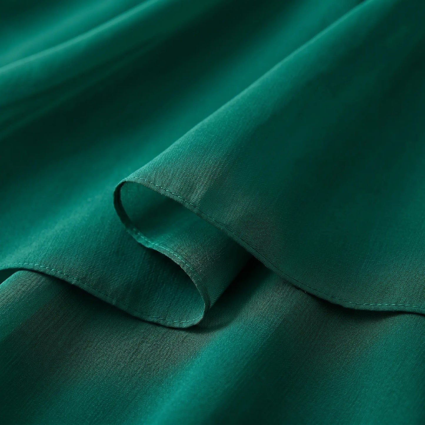 Close-up of the Kozumi A-Line midi dress's emerald green chiffon-blend fabric, showing its luxurious fluid drape, soft matte texture, and fine tonal stitching.
