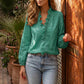 Woman modeling an emerald green Zokiru ruffled V-neck blouse with long sleeves and light wash jeans, standing casually next to a carved wooden door outdoors.