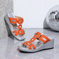 Eskari women's orange wedge sandals with geometric gold hardware and a textured silver platform sole, shown in a three-quarter view on a reflective surface.