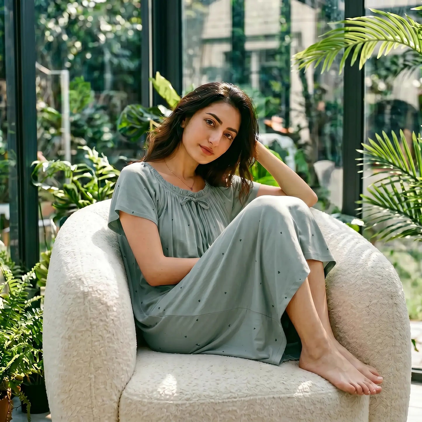 Model in Eucalyptus Green Zevryn modal lounge dress with gathered scoop neck, flutter sleeves, and micro-pointelle hearts, relaxing in a conservatory.
