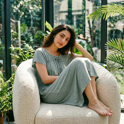 Model in Eucalyptus Green Zevryn modal lounge dress with gathered scoop neck, flutter sleeves, and micro-pointelle hearts, relaxing in a conservatory.