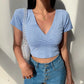 Model in a light blue Brivan floral wrap V-neck crop top with short sleeves, featuring a delicate white print, styled with blue high-waisted jeans and a gold necklace.