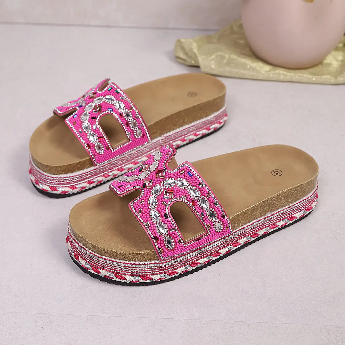 Fuchsia pink platform slide sandals featuring intricate bead and rhinestone embellishments on the straps, with a layered cork and woven midsole.