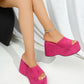 Vibrant fuchsia pink platform wedge sandals with a plush suede-like texture and single wide strap shown on a model's feet, featuring an ultra-high continuous wedge and open toe.