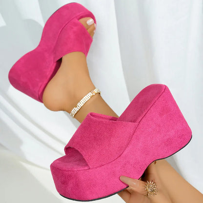 Vibrant fuchsia pink platform wedge sandals worn on a model's feet, showcasing the plush suede-like texture, single wide strap, and ultra-high continuous wedge.