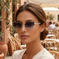 Woman wearing Galyth geometric cat-eye sunglasses with gold frames and gradient grey lenses, featuring crystal-embellished zigzag temples, in a vibrant outdoor cafe setting.
