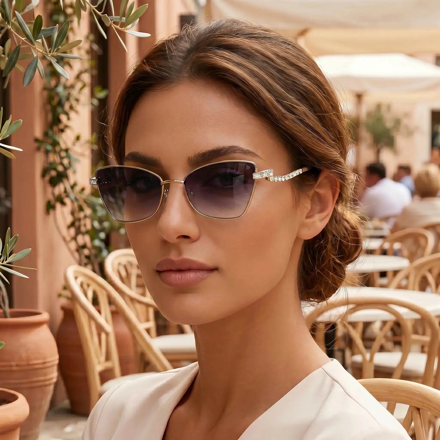 Woman wearing Galyth geometric cat-eye sunglasses with gold frames and gradient grey lenses, featuring crystal-embellished zigzag temples, in a vibrant outdoor cafe setting.