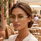 Woman wearing Galyth cat-eye sunglasses with gold frames and gradient amber lenses, featuring crystal-embellished zigzag temples, in an outdoor cafe setting.