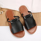 Geylan black flat slide sandals featuring a braided faux leather strap with a polished silver O-ring detail, presented in a studio setting on a textured mat.