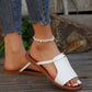A woman's feet wearing white Geylan flat braided strap summer slides with a polished silver O-ring accent, styled with distressed denim jeans.
