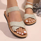 Elegant gold embellished flat sandals with shimmering crossover straps and elasticated ankle straps, shown on a woman's feet with white-painted toenails and a delicate anklet.